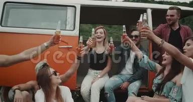 一群时髦的朋友在野餐聚会上喝着啤酒和欢呼声，坐在复古的货车后面